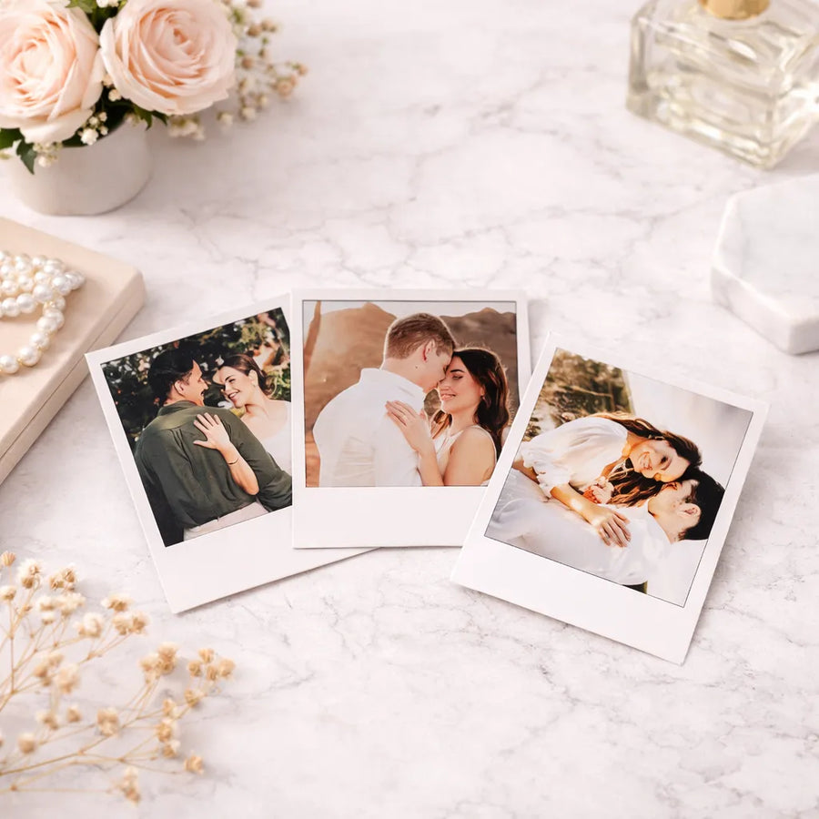 Three photo prints of a couple on a marble surface with flowers and a perfume bottle.
